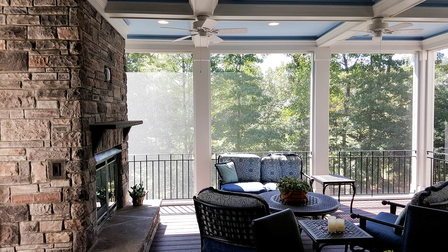 Screened porch with a stone fireplace, ceiling fans and wicker seating overlooking woods