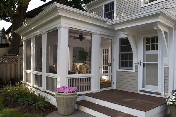 Screened porch with white columns and a ceiling fan built onto the side of a gray clapboard house